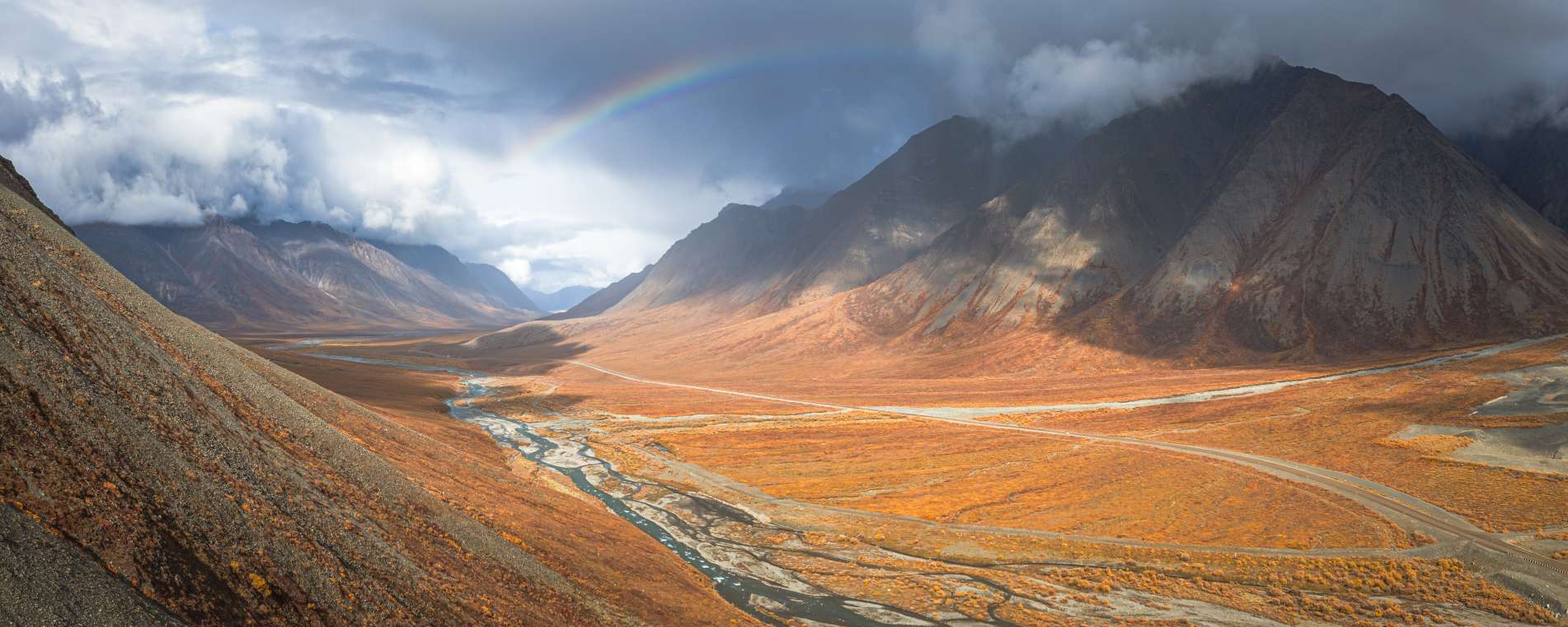 Aerial view of mountains and valley with rainbow and clouds