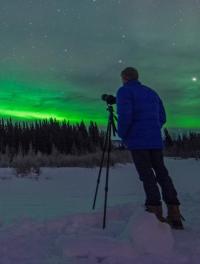 Photographer with tripod looking towards green aurora