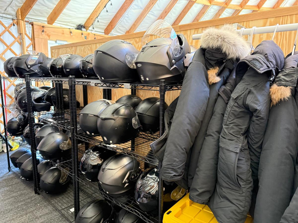 A rack of winter coats and snowmobiling helmets.