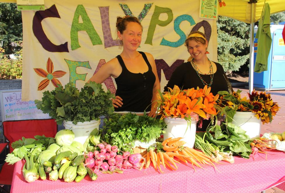 Two people standing in front of array of vegetables on table