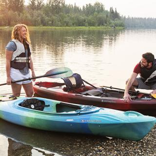 Two people smiling with their kayaks on the edge of the Chena River.