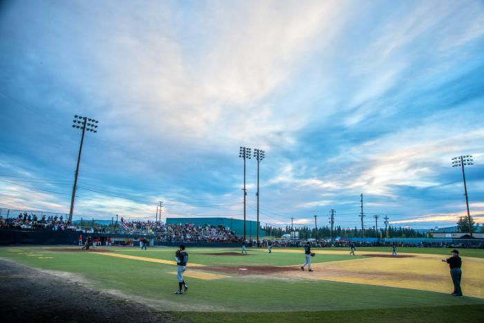 Sherman Hogue/Explore Fairbanks Baseball park with players on field during midnight sun season