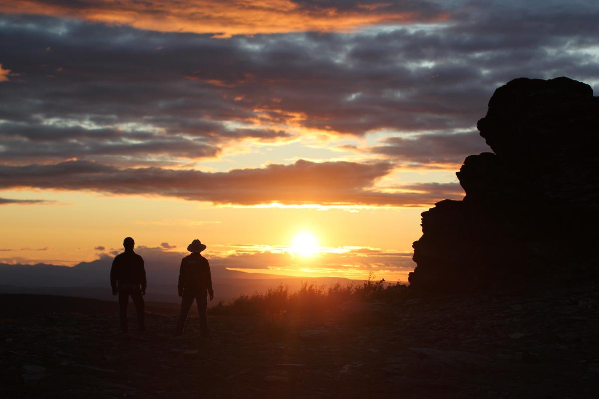 Two men watching sunset on the horizon with boulders in foreground