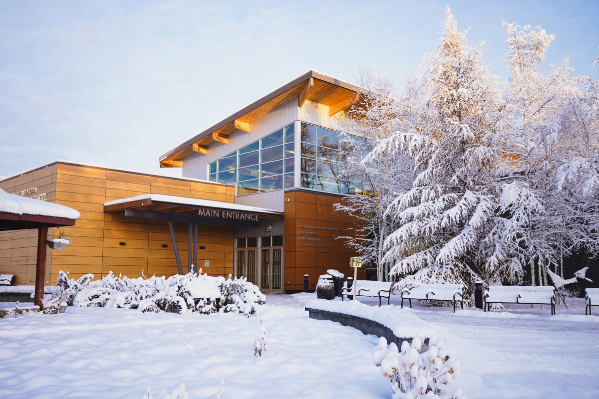 Morris Thompson Cultural and Visitors Center building in winter with snow covered ground and trees