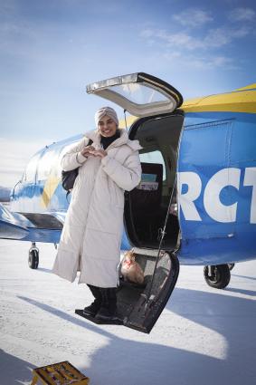 Person wearing a long parka, happily exiting an airplane from an arctic flightseeing tour.