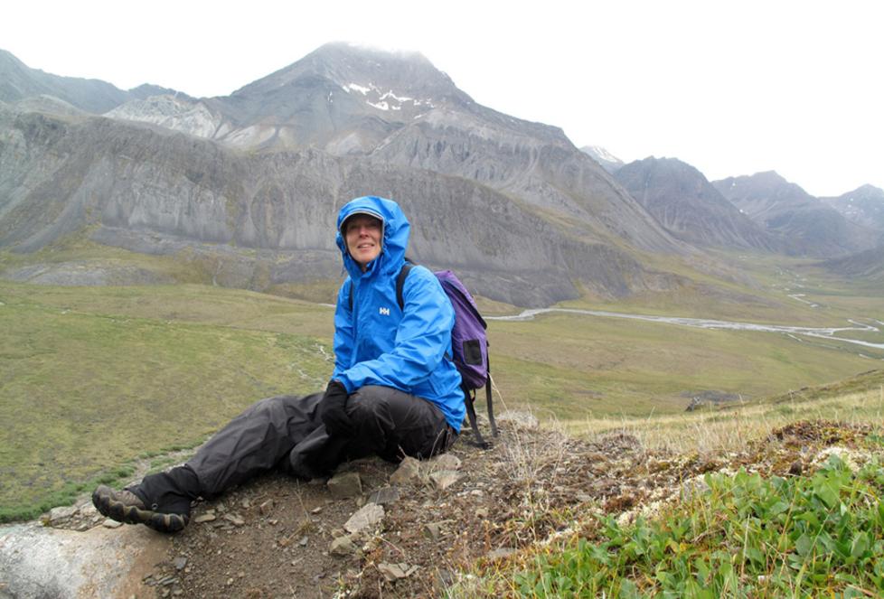 Hiker resting on ground with mountain towering in background and misty sky.