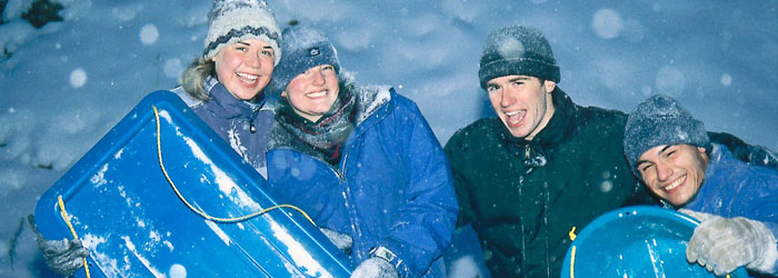 Four people laughing and smiling, holding blue sleds in snow