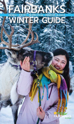 A smiling woman dressed in a lavender winter coat and colorful scarf gently holding the face of a reindeer in a snowy outdoor setting. Text overlay reads 'Fairbanks Winter Guide'.